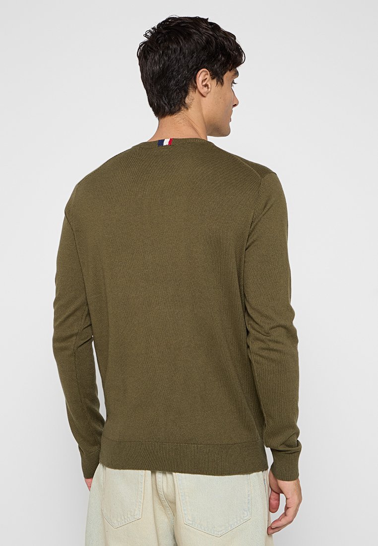Maglione a coste verde oliva con maniche lunghe, collo a giro e un piccolo dettaglio rosso, bianco e blu sul retro del colletto.