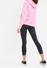 Roze hoodie met een kangoeroezak, gecombineerd met zwarte skinny jeans en zwarte sneakers met witte accenten.