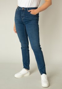 Donkerblauwe skinny jeans met een middelhoge taille, zijzakken en een klassiek vijfzakendesign, gecombineerd met witte sneakers.