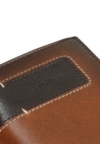 Brown leather wallet with black leather accents, featuring white stitching and a debossed logo, highlighting a smooth and textured finish.