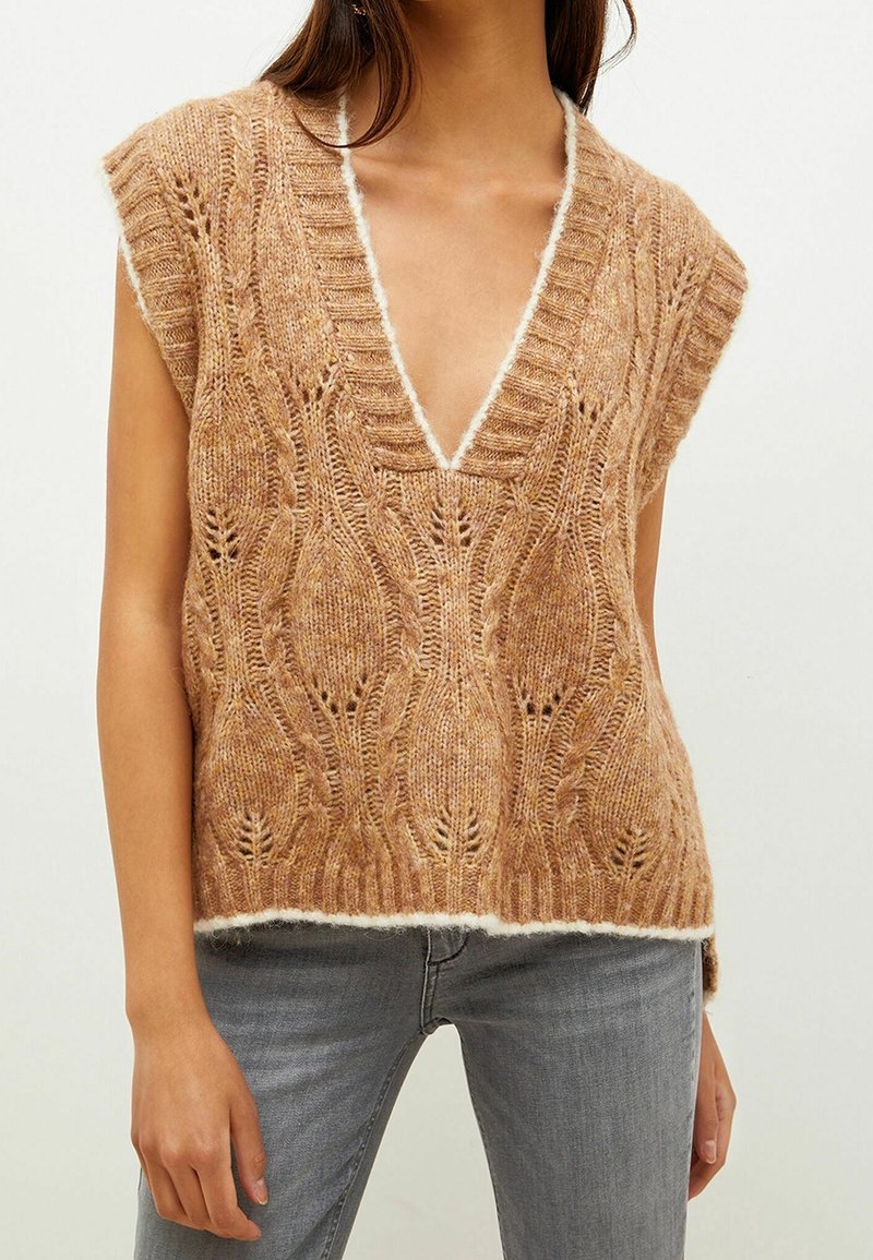 Strikket ærmeløs top i lysebrun med dyb V-hals. Tekstureret med et bladmønster og afsluttet med en cremefarvet kant.