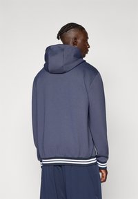 Sweatshirt com capuz em azul marinho escuro, apresentando um acabamento texturizado, punhos e bainha canelados com riscas brancas, e um ajuste descontraído.