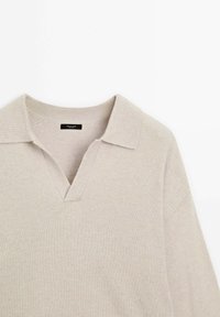 Pull tricot beige avec col en V et design à col. Présente un col et des bords de manches côtelés, une texture douce et un style minimaliste.