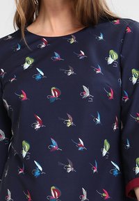 Haut bleu marine avec un col rond présentant un motif coloré de papillons en rouge, bleu, vert, jaune et blanc.