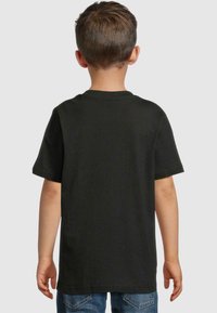 Sort bomulds T-shirt med korte ærmer, rund hals og ribbestrikket tekstur, set fra bagsiden. Parret med blå denim jeans.