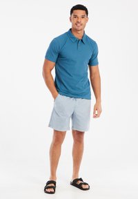 Blauwe katoenen polo met een kraag, gecombineerd met lichtblauwe shorts en zwarte sandalen. Eenvoudig ontwerp en casual pasvorm.