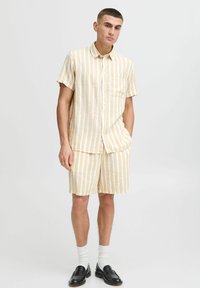 Camisa de manga corta, con botones y pantalones cortos a juego en rayas blancas y amarillas claras; fabricada con un tejido transpirable y un corte casual.