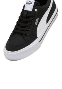 Sneaker nera Puma con striscia laterale bianca, suola in gomma bianca e lacci neri, inclinato per mostrare i dettagli superiori e laterali.