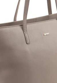 Grijze leren tote bag met een gestructureerd oppervlak, dubbele handvatten en een klein metalen logo-accent. Eenvoudig, minimalistisch ontwerp zonder externe zakken.