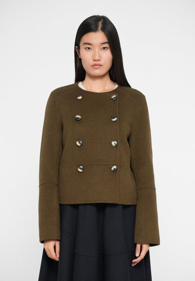 Olajzöld, dupla soros gyapjúzakó, nagy fekete gombokkal és széles ujjal, hozzáillő fekete, rakott szoknyával.