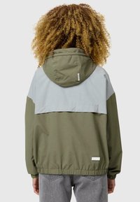 Tweekleurige gevoerde jas in olijfgroen en lichtgrijs, met elastische manchetten, een trekkoordcapuchon en een subtiele logo-patch op de zoom.