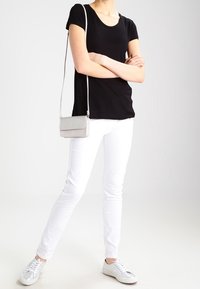 Černé tričko s krátkým rukávem, bílé skinny džíny, stříbrné tenisky a malá světlá šedá crossbody kabelka. Jednoduchý, přiléhavý design.