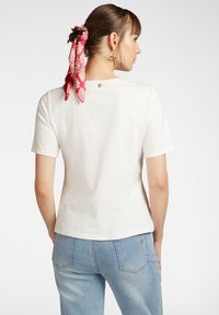 Maglietta bianca a maniche corte con un design semplice, caratterizzata da un piccolo logo sulla parte superiore della schiena e una texture liscia e morbida.