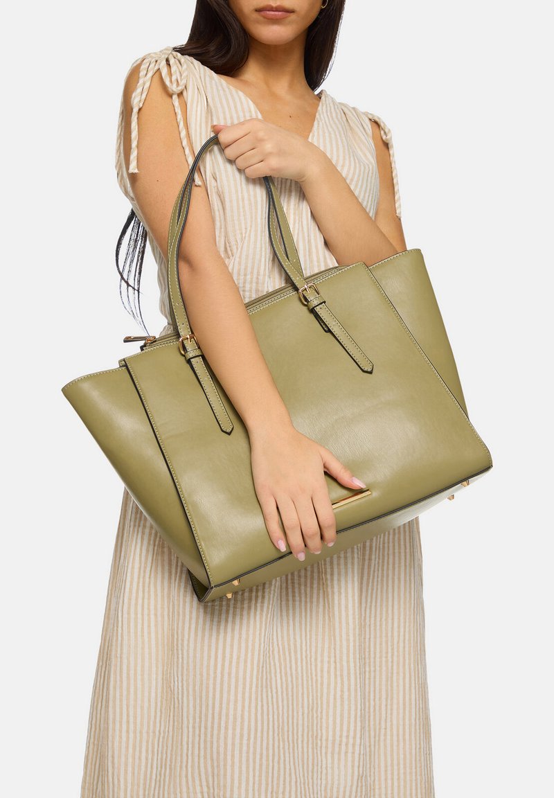 Sac fourre-tout en cuir vert avec une forme structurée, deux poignées robustes et des accents en métal doré. Texture lisse avec des coutures contrastées.