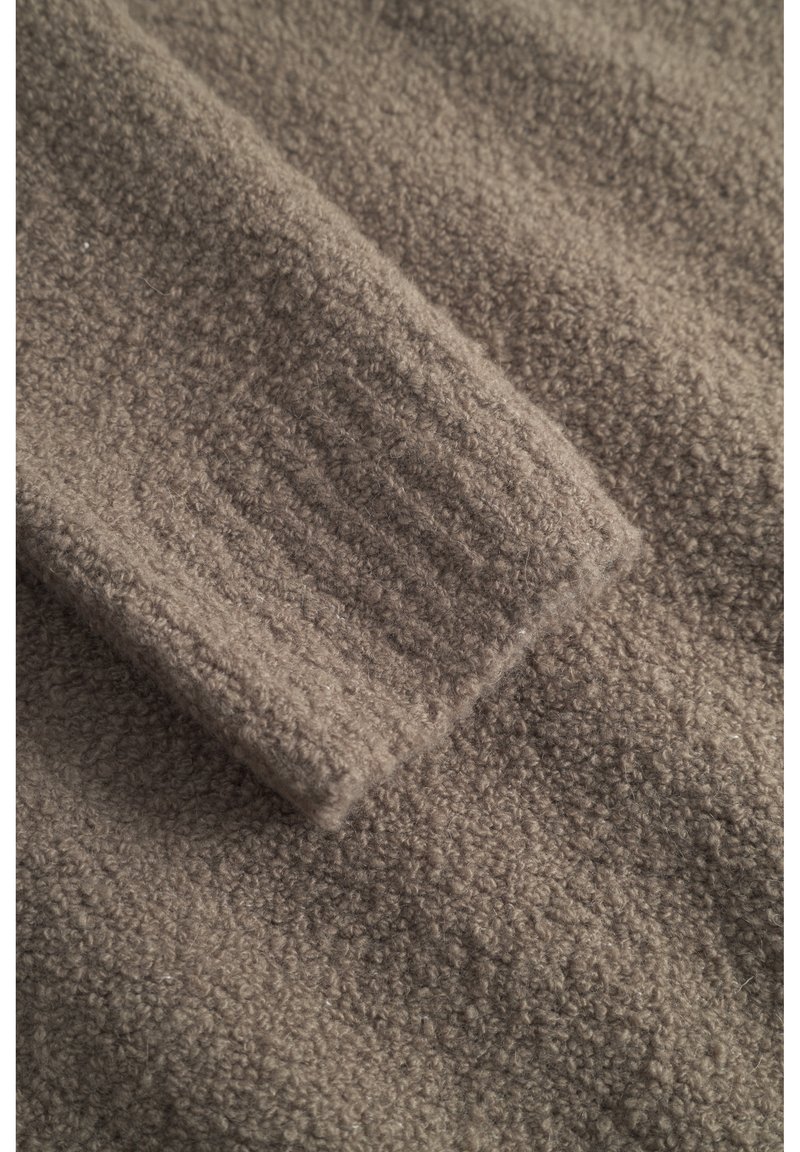 Tissu en polaire marron avec une surface texturée et douce, présentant un détail en maille côtelée sur le bord. Apparence chaude et confortable.