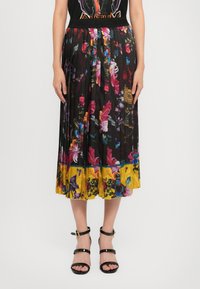 Gonna midi plissettata con una base nera e motivi floreali colorati, orlo giallo vivace e vita elastica. Abbinata a sandali neri.
