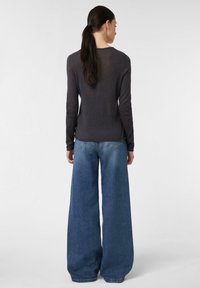 Dunkelgrauer Langarmpullover kombiniert mit weit geschnittenen blauen Jeans. Der Stoff wirkt weich und leicht strukturiert, was den lässigen Stil unterstreicht.