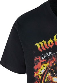 Černé bavlněné tričko s grafickým designem v ohnivých červených a žlutých akcentách, na kterém je text "MOTÖR" a výbušná grafika.