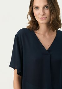 Blusa blu navy con maniche corte e fluide, scollatura a V e un tessuto morbido e leggero. Design semplice senza fantasie o hardware.