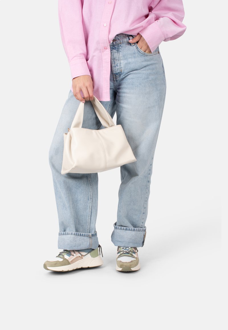 Borsa in pelle bianca con manici corti, texture liscia e forma arrotondata, tenuta in una mano, abbinata a jeans azzurri chiari e sneakers.