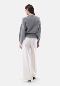 Grau gestrickter Pullover mit Rundhalsausschnitt, Ballonärmeln und schmalem Saum, kombiniert mit weißen weiten Hosen und schwarzen High Heels.