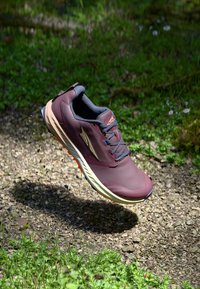 Burgundowe buty biegowe z szarymi akcentami, teksturowana siateczka na cholewce oraz jasna podeszwa. Detale obejmują widoczne sznurówki i pomarańczową podeszwę.