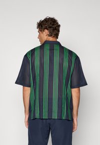 Marine blå mesh kortermet skjorte med grønne vertikale striper. Bakdelen har et lett design med en avslappet passform og krage.