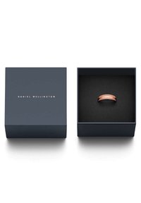 Vaaleanpunakulta sormus esillä tummansinisessä laatikossa, jossa on kultateksti. Laatikossa on teksturoitu musta sisus, joka korostaa sormuksen kiiltävää viimeistelyä.