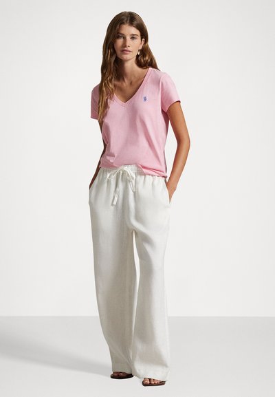 T-shirt en coton rose clair à col en V associé à un pantalon en lin blanc ample. Les détails notables incluent un petit logo sur le t-shirt et une taille à cordon.