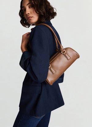 Borsa a tracolla in pelle marrone con design strutturato, caratterizzata da due cinturini frontali e una tracolla. Indossata con un blazer scuro su uno sfondo neutro.