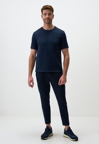 T-shirt corto da uomo in navy con colletto a girocollo, abbinato a pantaloni aderenti dello stesso colore. Entrambi sono realizzati in un tessuto liscio e elastico.