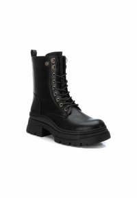 Bota de piel negra hasta el tobillo con puntera redonda, parte delantera con cordones, acentos metálicos decorativos y suela de goma gruesa y con patrón.