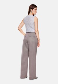 Light gray lace knit sleeveless top with a high neckline, paired with high-waisted, wide-leg gray striped trousers featuring two back pockets.