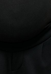 Gros plan d'une personne portant des vêtements en tissu noir avec un détail de poche visible sur le côté inférieur droit.