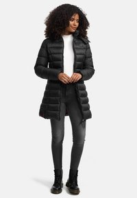 Doudoune noire avec un matelassage horizontal, fermeture éclair et capuche réglable. Associée à un jean gris et des bottes noires à lacets.