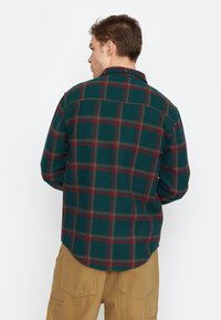 Groene geruite flanellen shirt met rode en gele accenten, voorzien van een klassieke kraag en een afgeronde zoom. Achteraan zichtbaar met een comfortabele pasvorm en lange mouwen.