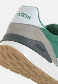 Grüner und grauer Sportschuh mit Gummisohle, Wildlederakzenten und weißer Ferse sowie "adidas"-Markierung an der Seite.
