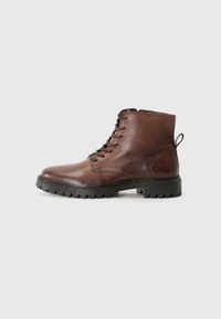 Bottines en cuir marron avec une semelle en caoutchouc noir texturé et des lacets, présentées sur un fond blanc uni.