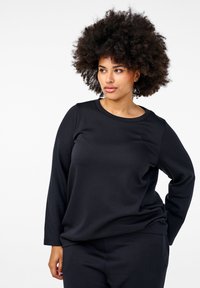 Svart långärmad t-shirt gjord av mjukt material, med rund halsringning och avslappnad passform. Kombineras med matchande mörka byxor.