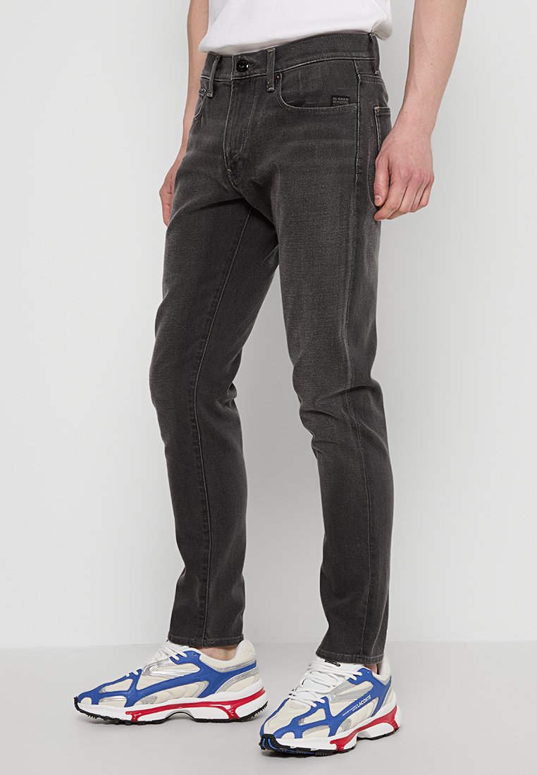 Donkergrijze denim jeans met een slim fit, vijf-pocket ontwerp en metalen knoopsluiting, gecombineerd met witte en blauwe sneakers.