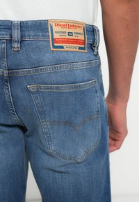 Jeans de mezclilla azul claro con una etiqueta de cuero en la pretina, que presentan detalles de costura en los bolsillos traseros y un ajuste relajado.