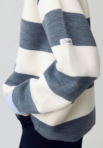 Maglione a righe con bande alternate blu navy e crema, caratterizzato da una texture morbida e un accento blu chiaro ai polsini. Etichetta del brand visibile.