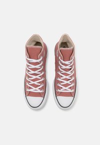 Par av rosa högskärning kanvas sneakers med vita gummitåspetsar och vita snören, sedd uppifrån på en vit bakgrund.