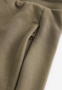 Leggings de sport vert olive avec une texture lisse et un détail de fermeture éclair sur le côté. Présentent un design ajusté et des coutures soignées.