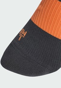 Melnas un oranžas svītras zeķe ar ribotu struktūru. Tai ir apaļa pirksta daļa un neliels oranžs logotips netālu no pirksta zonas.