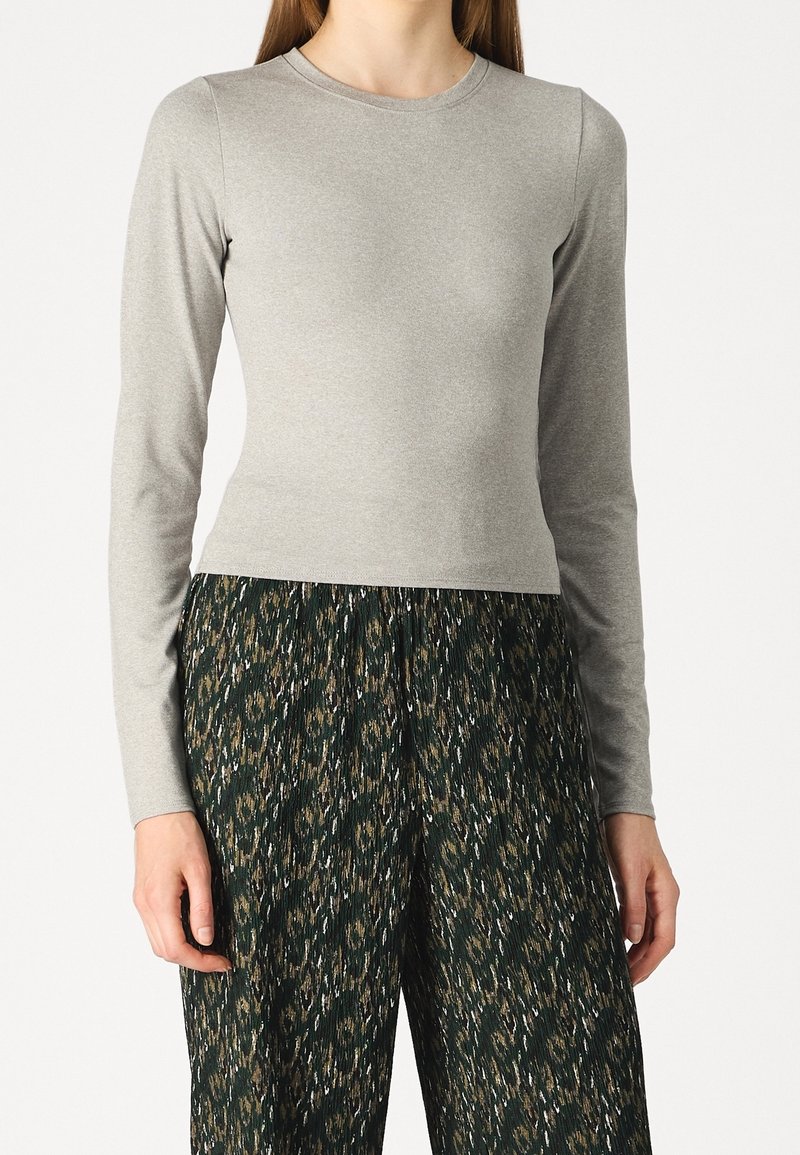 Woman wearing a fitted light gray long-sleeve top and loose dark green pants with an abstract leopard print pattern.