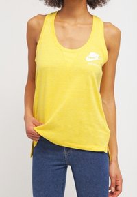 Geel tanktop gemaakt van zachte, lichte stof met een ronde halslijn en zijsplitten. Bevat het witte Nike-logo en de tekst "JUST DO IT."