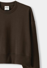 Brun kort sweatshirt med ribbad halsringning och ärmmuddar. Slät textur, design med drop shoulder, med en etikett vid halsringningen.