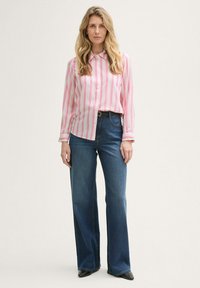 Triibuline roosa ja valge nööpidega särk tumedate siniste laiendatud teksadega. Komplekti kuuluvad must vöö ja terava ninaga mustad kingad.