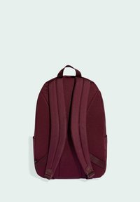 Mochila burdeos con correas acolchadas, textura de tela, dos bolsillos laterales y un asa superior para llevar fácilmente. Diseño simple y depurado.